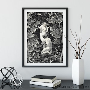 May include: Black and white framed art print depicting two figures in a forest setting. The artwork features detailed linework, with one figure kneeling before another. The print is displayed on a black surface with decorative objects and books.
