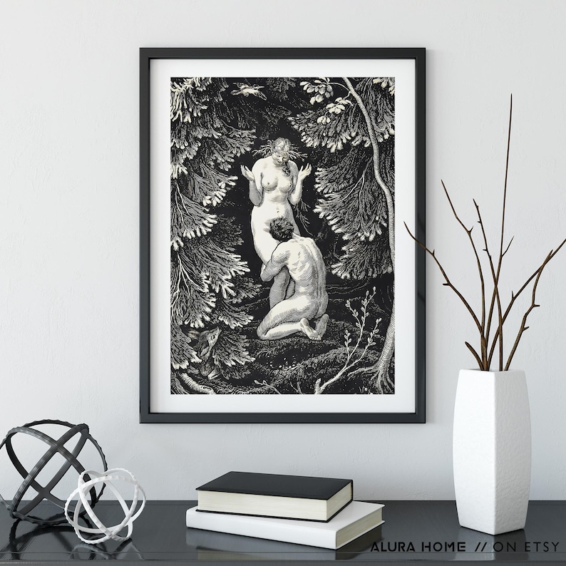 May include: Black and white framed art print depicting two figures in a forest setting. The artwork features detailed linework, with one figure kneeling before another. The print is displayed on a black surface with decorative objects and books.