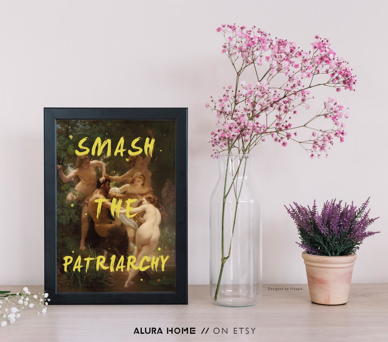 May include: A black framed print featuring a painting of a group of people in a woodland setting. The words "SMASH THE PATRIARCHY" are written in yellow over the painting.