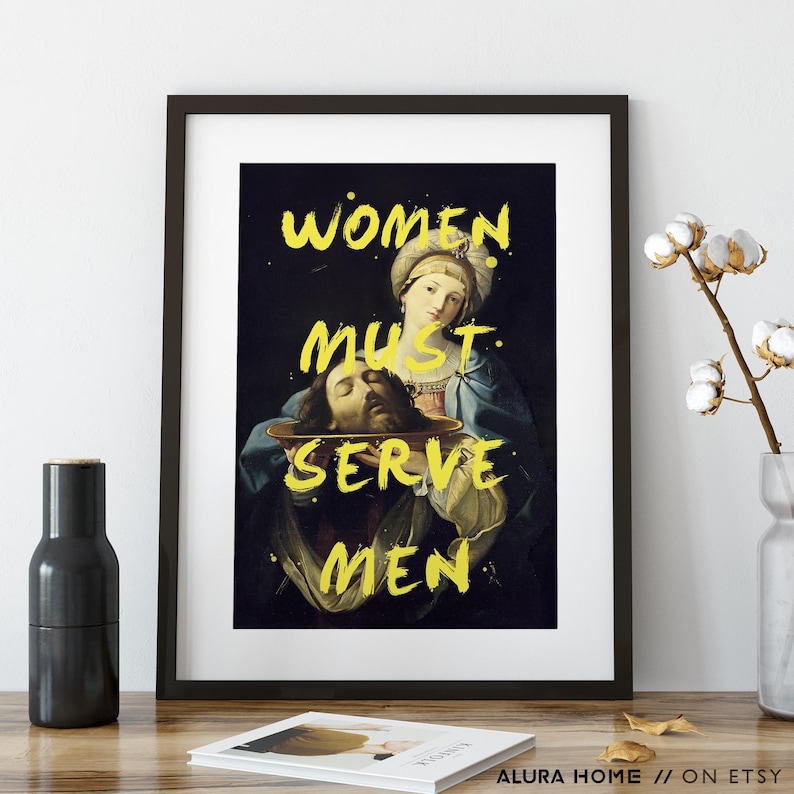 May include: Framed art print featuring a classical painting with the text "WOMEN MUST SERVE MEN" in yellow. The artwork depicts a woman holding a platter with a severed head. The print is in a black frame.