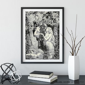 May include: Black and white framed art print featuring a detailed illustration of two mermaids in a watery environment. One mermaid is looking up, while the other is reaching out. The art print is displayed on a black surface with decorative items.