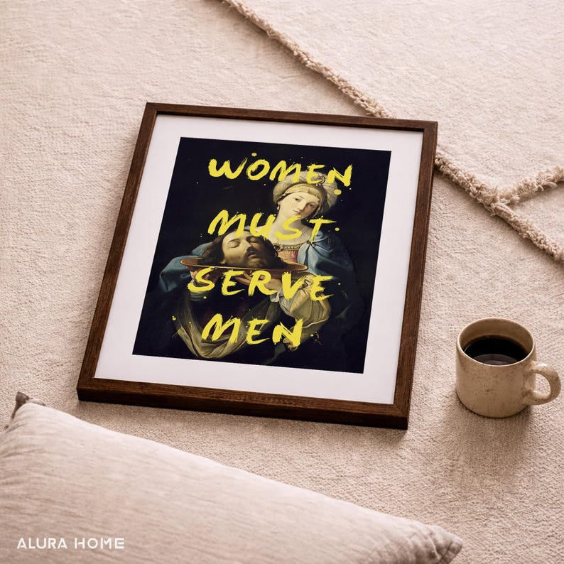 May include: Framed art print with a dark background featuring a Renaissance-style painting. The text "WOMEN MUST SERVE MEN" is overlaid in yellow. A beige mug with coffee sits to the right.