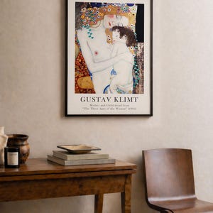 May include: A framed art print featuring Gustav Klimt's Mother and Child detail from The Three Ages of the Woman (1905). The artwork displays a pale figure embracing a child, surrounded by decorative gold, blue, and red patterns on a black background.