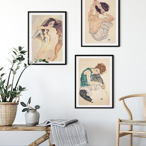 May include: Three black framed art prints of nude figures in various poses. The prints are hung on a white wall with a wooden bench and a chair in the foreground.