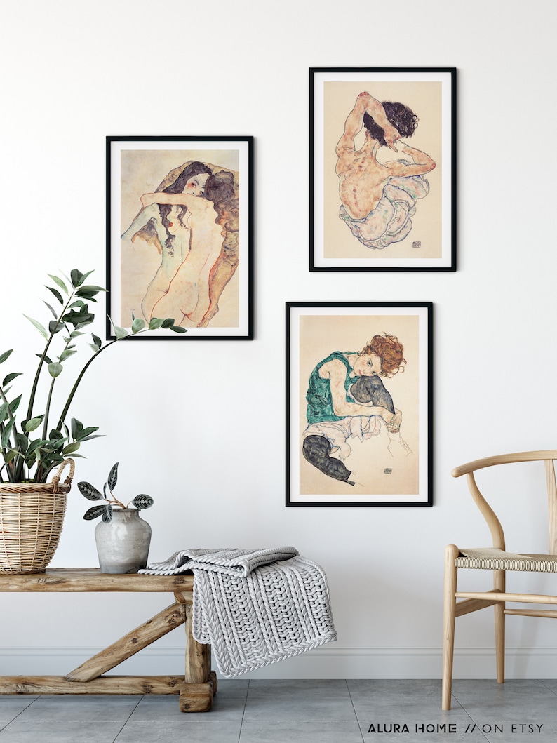 May include: Three black framed art prints of nude figures in various poses. The prints are hung on a white wall with a wooden bench and a chair in the foreground.