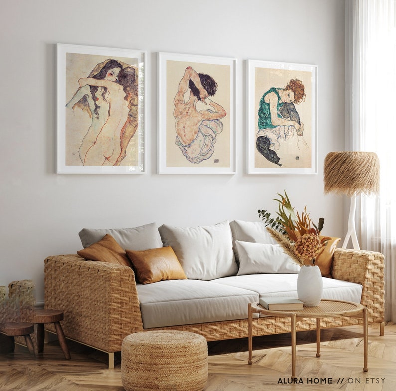 May include: Three framed art prints featuring nude figures in various poses. The prints are hung on a white wall above a wicker sofa with brown throw pillows.