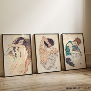 May include: Three framed black and white art prints of nude figures in various poses. The prints are set against a white wall.