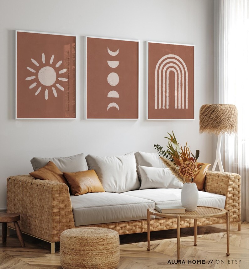 May include: Three framed wall art prints featuring white line drawings on a terracotta background. The left print shows a sun, the center print displays moon phases, and the right print depicts a rainbow arch. The text ALURA HOME // ON ETSY is visible.