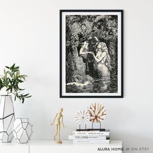 May include: Black framed art print featuring a detailed black and white illustration of two mermaids in a watery environment, surrounded by foliage. The artwork is displayed on a white wall, with decorative items in the foreground.