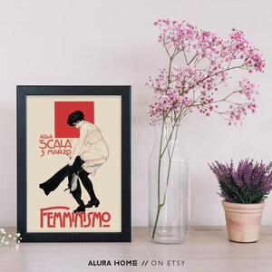 May include: A black framed print with a vintage poster design featuring a woman in a white dress and black stockings. The poster text reads "Alla Scala 3 Marzo Femminismo".