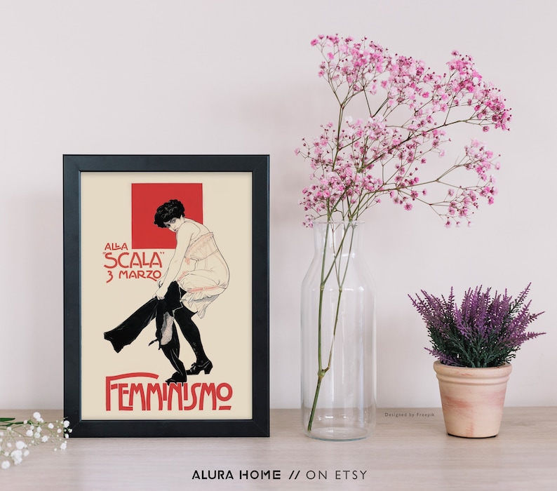 May include: A black framed print with a vintage poster design featuring a woman in a white dress and black stockings. The poster text reads "Alla Scala 3 Marzo Femminismo".