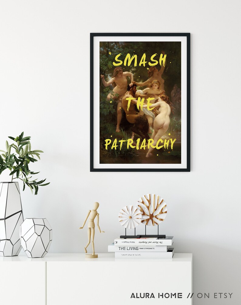 May include: A framed art print featuring a painting of a group of people in a woodland setting. The words "SMASH THE PATRIARCHY" are written in yellow paint across the image.