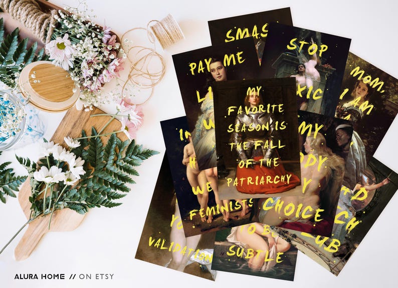 May include: A collection of art prints with yellow text on dark backgrounds. The prints feature classical paintings with overlaid phrases like "My favorite season is the fall of the patriarchy." Floral arrangements and decorative items surround the prints.