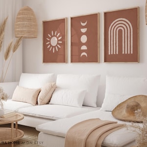 May include: Three framed wall art prints featuring a terracotta background with white line art illustrations. The left print shows a sun, the center print displays moon phases, and the right print depicts a rainbow arch. The text ALURA HOME // ON ETSY is visible.
