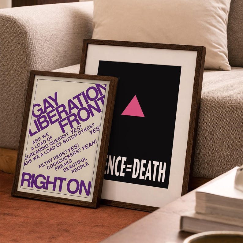May include: Two framed posters with dark wood frames. The left poster has a white background with purple text reading GAY LIBERATION FRONT, RIGHT ON, and other phrases. The right poster has a black background with a pink triangle and SILENCE=DEATH.