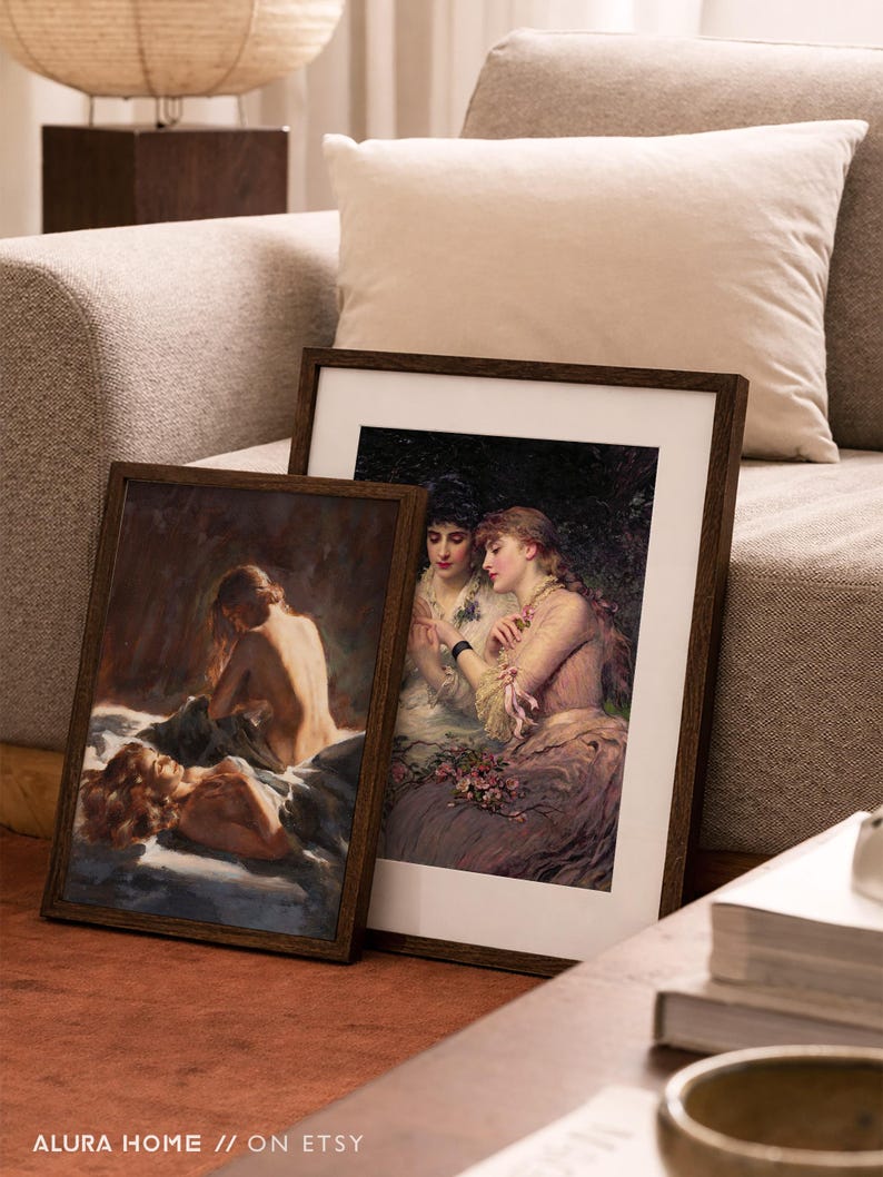 Pode incluir: Duas impress&otilde;es de arte emolduradas com pinturas cl&aacute;ssicas, encostadas em um sof&aacute;. As impress&otilde;es apresentam mulheres em um cen&aacute;rio rom&acirc;ntico, com molduras de madeira escura. O texto "ALURA HOME // ON ETSY" &eacute; vis&iacute;vel na parte inferior.