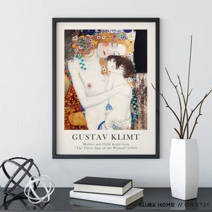 May include: A framed art print featuring Gustav Klimt's Mother and Child detail from The Three Ages of the Woman (1905). The artwork displays a pale woman with long reddish hair holding a small child, surrounded by decorative gold and floral patterns.
