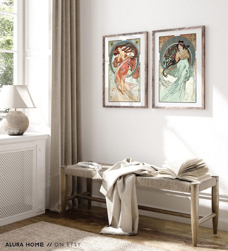 Puede incluir: Dos impresiones art&iacute;sticas enmarcadas con ilustraciones de estilo Art Nouveau de mujeres con cabello suelto y fondos florales ornamentados. Las impresiones est&aacute;n en marcos de madera y cuelgan de una pared blanca. Un banco con una parte superior tejida y una manta est&aacute;n frente a la pared.