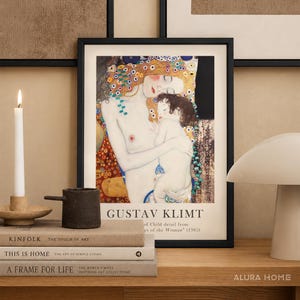 May include: A framed art print featuring Gustav Klimt's The Three Ages of Woman, specifically the Mother and Child detail. The print is housed in a black frame and displays the artist's name and title text at the bottom in a clean, sans-serif font.
