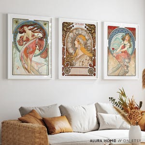 Puede incluir: Tres l&aacute;minas de arte enmarcadas con ilustraciones al estilo de Alphonse Mucha. La l&aacute;mina de la izquierda muestra a una mujer en un marco circular, la central muestra a una mujer con el texto LA PLUME y la de la derecha a una mujer sosteniendo una flor.