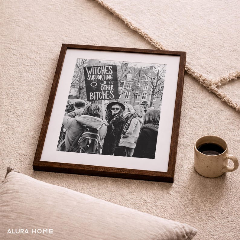 K&ouml;nnte beinhalten: Gerahmtes Schwarz-Wei&szlig;-Foto einer Demonstration. Das Schild lautet "Witches Supporting Other Bitches". Rechts vom Rahmen befindet sich eine Keramiktasse mit Kaffee. Der Rahmen ist dunkelbraun.