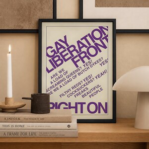 May include: A rectangular black-framed wall art print featuring bold purple text on a cream background. The text reads GAY LIBERATION FRONT, ARE WE A LOAD OF SCREAMING QUEENS? YES! ARE WE A LOAD OF BUTCH DYKES? YES! FILTHY REDS? YES! COCKSUCKERS? YEAH! FREAKS BEAUTIFUL PEOPLE RIGHT ON.