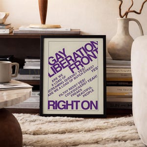 May include: A framed poster with a cream background and bold purple text that reads: GAY LIBERATION FRONT, ARE WE A LOAD OF SCREAMING QUEENS? YES! ARE WE A LOAD OF BUTCH DYKES? YES! FILTHY REDS? YES! COCKSUCKERS? YEAH! FREAKS BEAUTIFUL PEOPLE RIGHT ON.