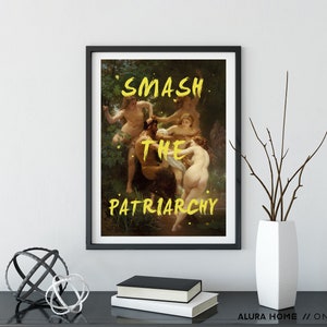 May include: A black framed print featuring a painting of a group of people in a woodland setting. The words "SMASH THE PATRIARCHY" are written in yellow paint across the image.
