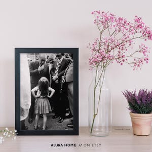Peut inclure: Une photographie encadr&eacute;e en noir et blanc d'une petite fille devant un groupe d'hommes en costume. Le cadre est noir. Un vase en verre transparent avec des fleurs roses et une petite plante de lavande en pot sont &agrave; droite. Texte en bas : "ALURA HOME // ON ETSY."