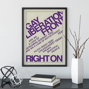 May include: A framed poster with a cream background and bold purple text that reads GAY LIBERATION FRONT, ARE WE A LOAD OF SCREAMING QUEENS? YES! ARE WE A LOAD OF BUTCH DYKES? YES! FILTHY REDS? YES! COCKSUCKERS? YEAH! FREAKS BEAUTIFUL PEOPLE RIGHT ON.