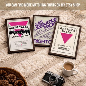 May include: Three framed posters featuring historical LGBTQ+ activism graphics. The left poster displays a pink triangle and text reading Come Out... Come Out... wherever you are. The center poster features purple text reading GAY LIBERATION FRONT. The right poster shows a pink triangle and text reading GAY PRIDE WEEK.