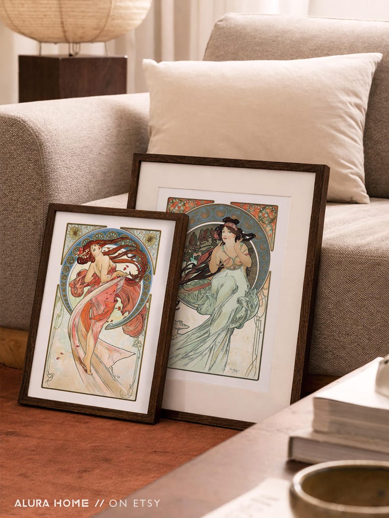 Puede incluir: Dos impresiones art&iacute;sticas enmarcadas con ilustraciones de estilo Art Nouveau de mujeres con cabello suelto y fondos florales. Los marcos marr&oacute;n oscuro est&aacute;n sobre una superficie marr&oacute;n cerca de un sof&aacute;.