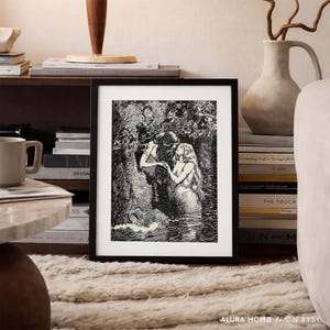 May include: Black and white framed art print depicting two figures in a forest setting. One figure is reaching towards the other, who is standing in water. The art print is displayed on a shelf with books and a mug.