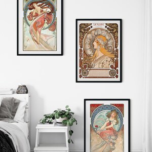 Puede incluir: Tres l&aacute;minas de arte enmarcadas con ilustraciones al estilo de Alphonse Mucha. La l&aacute;mina superior izquierda muestra a una mujer con un vestido rosa fluido, la superior derecha titulada La Plume muestra a una mujer de perfil y la inferior derecha muestra a una mujer sentada.