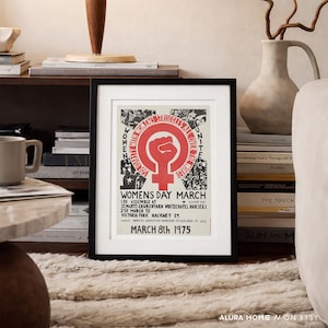 Puede incluir: P&oacute;ster enmarcado con borde negro. El p&oacute;ster presenta un pu&ntilde;o rojo dentro de un c&iacute;rculo con las palabras "WOMEN'S STRUGGLES ALL OVER THE WORLD UNITE" y "WOMENS DAY MARCH" con la fecha "MARCH 8th 1975".