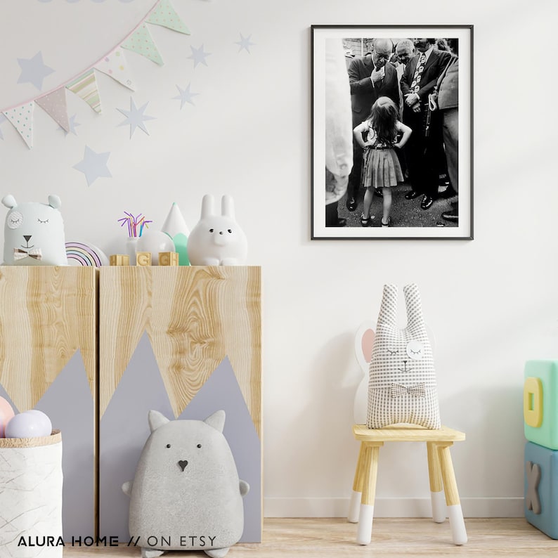 Peut inclure: Photographie encadr&eacute;e en noir et blanc d'une jeune fille, les mains sur les hanches, entour&eacute;e d'hommes en costume. La photo est affich&eacute;e sur un mur blanc dans une chambre d'enfant, avec des objets d&eacute;coratifs.