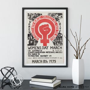 Puede incluir: Un p&oacute;ster enmarcado con borde negro. El p&oacute;ster tiene un dise&ntilde;o rojo y blanco con el texto "WOMENS DAY MARCH" y "SOLIDARITY WITH WOMEN'S STRUGGLES ALL OVER THE WORLD". Tambi&eacute;n es visible la fecha "MARCH 8th 1975".