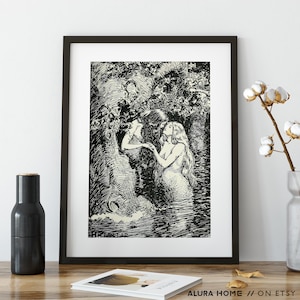 May include: Black and white framed art print depicting two mermaids in a forest setting. One mermaid has long flowing hair and is partially submerged in water. The other mermaid is reaching out. The print is in a black frame.