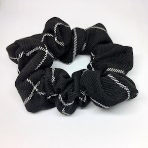 May include: A black scrunchie with a white plaid design. The hair accessory is made of a soft fabric and is designed to hold hair in place. The scrunchie is a stylish and practical accessory for various hairstyles.
