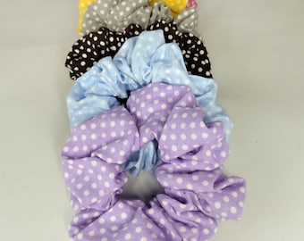 May include: A selection of scrunchies in shades of purple, light blue, brown, grey, and yellow. Each scrunchie is adorned with a white polka dot design. These fabric scrunchies are suitable for a variety of hairstyles.