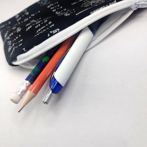 May include: A black pencil case with a white zipper, filled with a pencil, pen, and a pencil. The case is patterned with white mathematical equations. The pencil is orange, the pen is white and blue, and the other pencil is green and blue.