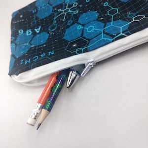 May include: A pencil case with a white zipper, featuring a blue and black geometric pattern. Inside, a red pencil, a patterned pencil, and a pen are partially visible. The case is designed for storing writing instruments.