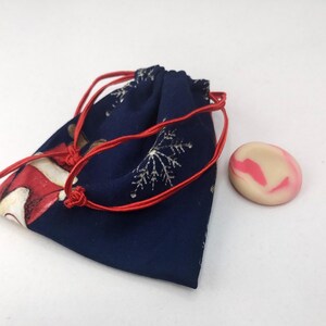 Puede incluir: Una bolsa azul marino con cordón rojo y un estampado festivo de Papá Noel y copos de nieve. Una pequeña piedra ovalada rosa y blanca está al lado de la bolsa. La bolsa está cerrada.