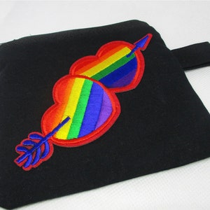 May include: Black pouch featuring two rainbow-coloured hearts pierced by a blue arrow. The hearts are embroidered with red outlines. The pouch has a small black strap.