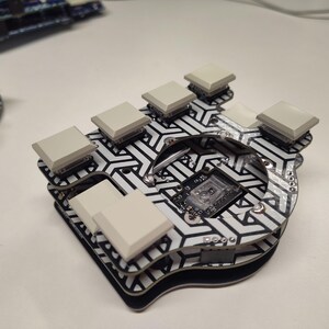 May include: A custom mechanical keyboard with a black and white geometric pattern. It features several light gray keycaps and a small circuit board. The keyboard is designed for ergonomic use.