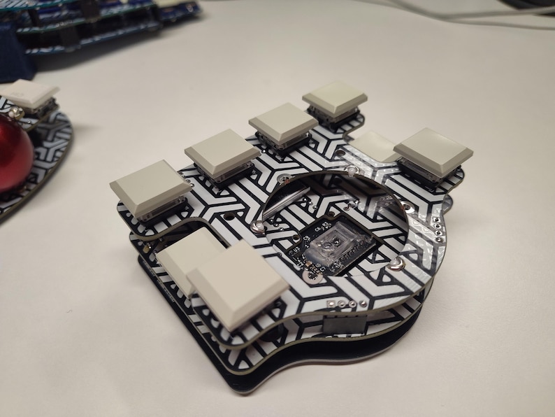 May include: A custom mechanical keyboard with a black and white geometric pattern. It features several light gray keycaps and a small circuit board. The keyboard is designed for ergonomic use.