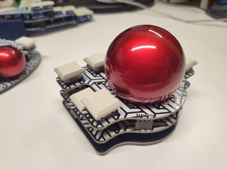 May include: A red, glossy sphere sits atop a custom-built keyboard with square, off-white keycaps. The keyboard has a black and white geometric pattern. The design is modern and unique.