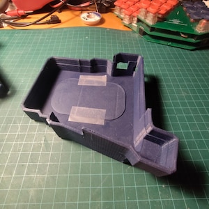 Könnte beinhalten: Ein dunkelblaues, 3D-gedrucktes Kunststoffgehäuse mit einer rechteckigen Öffnung und einer kleineren Öffnung an der Seite. Das Gehäuse ist mit einem Stück Klebeband abgeklebt.