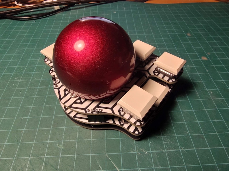 May include: A deep red, spherical object rests on a black and white patterned base, surrounded by several square, off-white blocks. The base has a unique, curved shape. The background is a green grid.