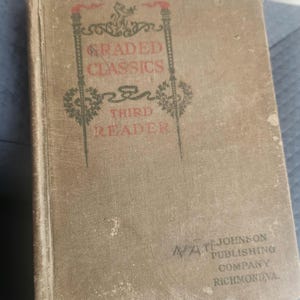 Op de afbeelding: Een vintage, groen, gebonden boek getiteld "Graded Classics Third Reader" met de uitgever "B.F. Johnson Publishing Company Richmond, VA" gedrukt in de rechterbenedenhoek.